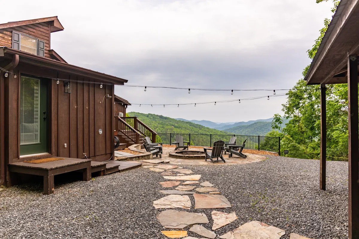 A charming outdoor seating area featuring stone pathways, Adirondack chairs, string lights, and a wide mountain view. The ambience is magical and tranquil, ideal for evening socializing, morning coffee, and nighttime stargazing.