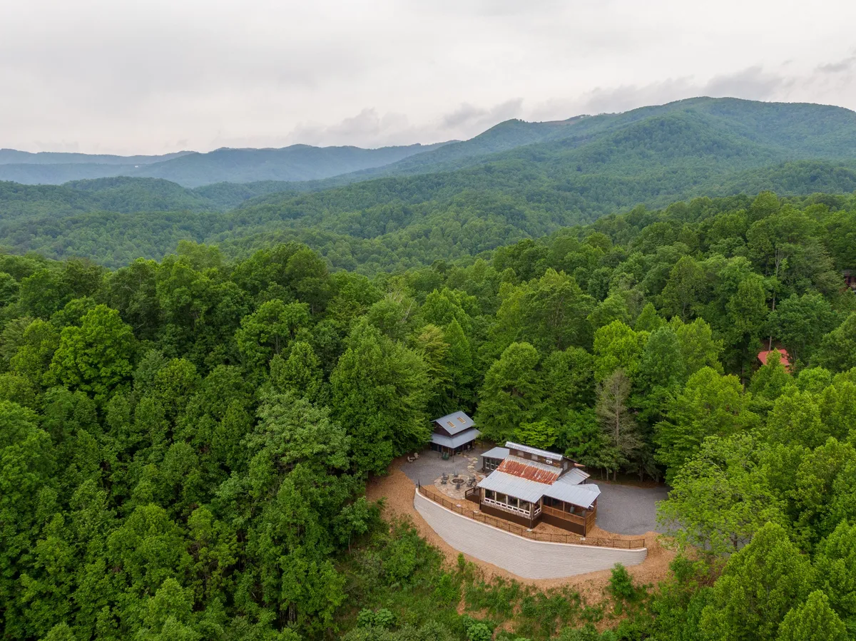 The rustic cabin is framed by lush greenery and majestic mountains in the distance. This wide-angle shot establishes the property’s secluded, peaceful setting, surrounded by nature’s beauty and ideal for focused work.
