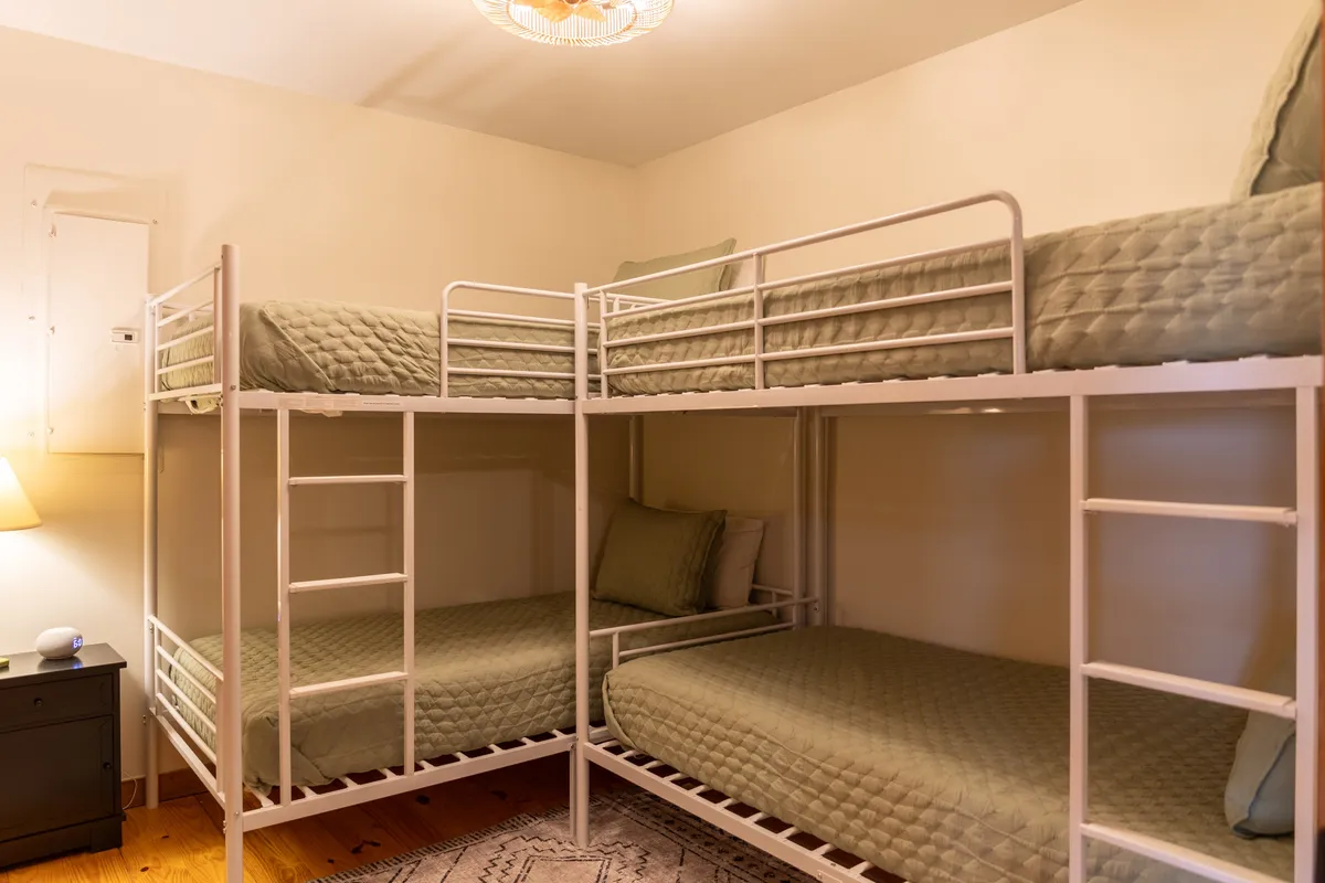 A cheerful bunk room highlighted by two sets of twin-over-twin bunk beds, a central nightstand with a lamp, and playful bedding. The arrangement is inviting for children or young guests, encouraging both rest and late-night chats.