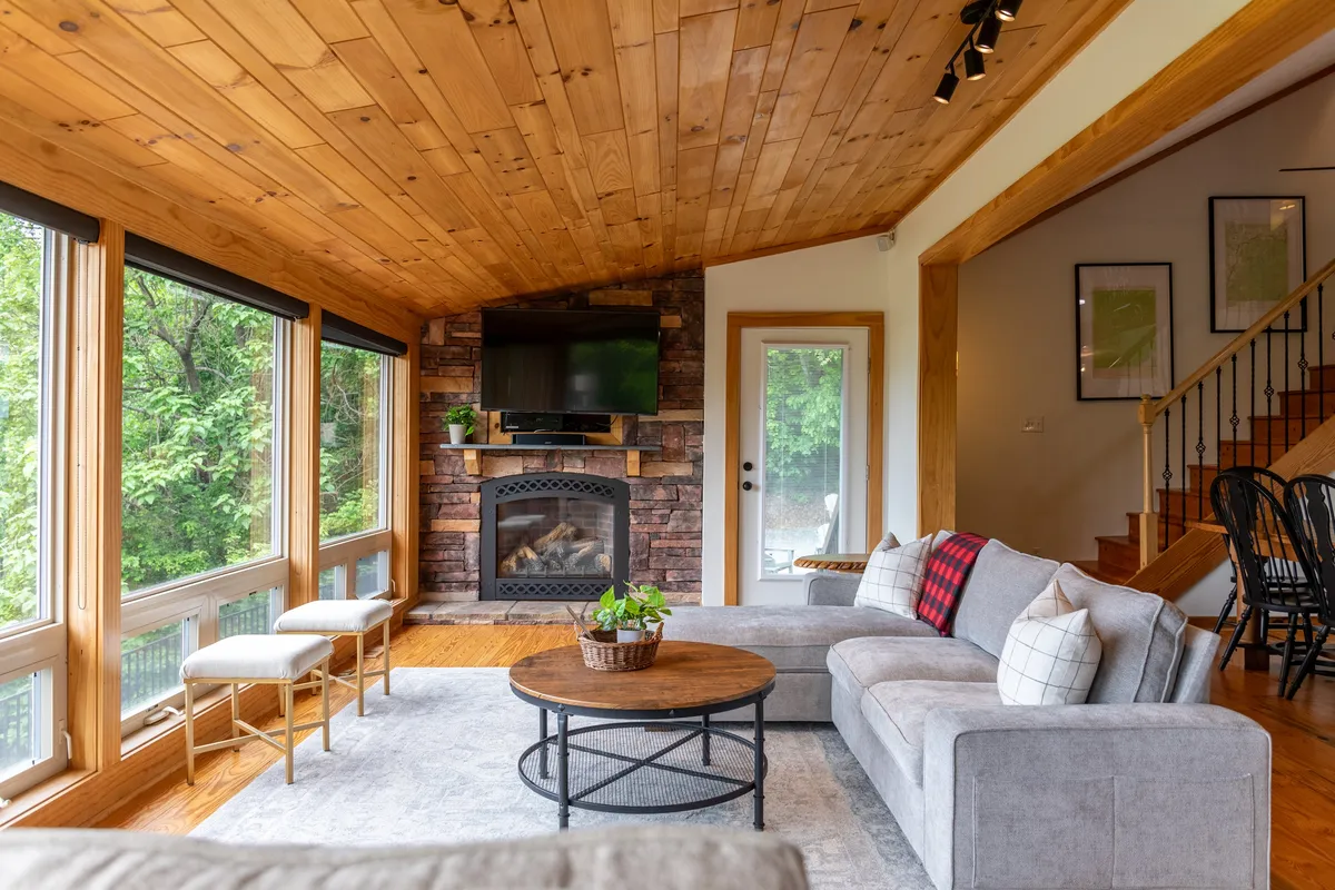 This image features a spacious living room with a plush sofa arranged around a coffee table, a prominent fireplace, and expansive windows that draw in natural light and reveal scenic mountain views. The cozy setup encourages relaxation and socializing, with the fireplace and large windows serving as focal points.
