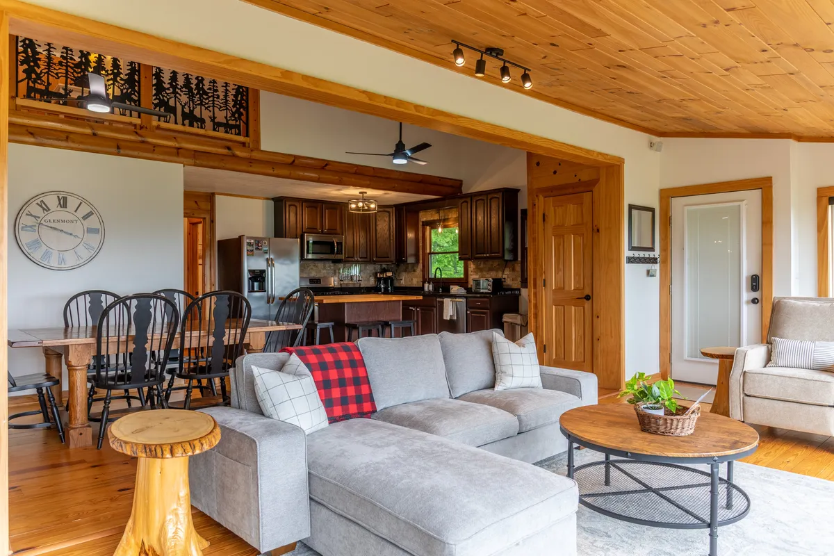 This image shows a welcoming great room with a sectional sofa, wooden dining table for six, and a modern, well-equipped kitchen in the background. Decorative touches and natural lighting create a cozy, lived-in feel, perfect for family gatherings or casual mornings.