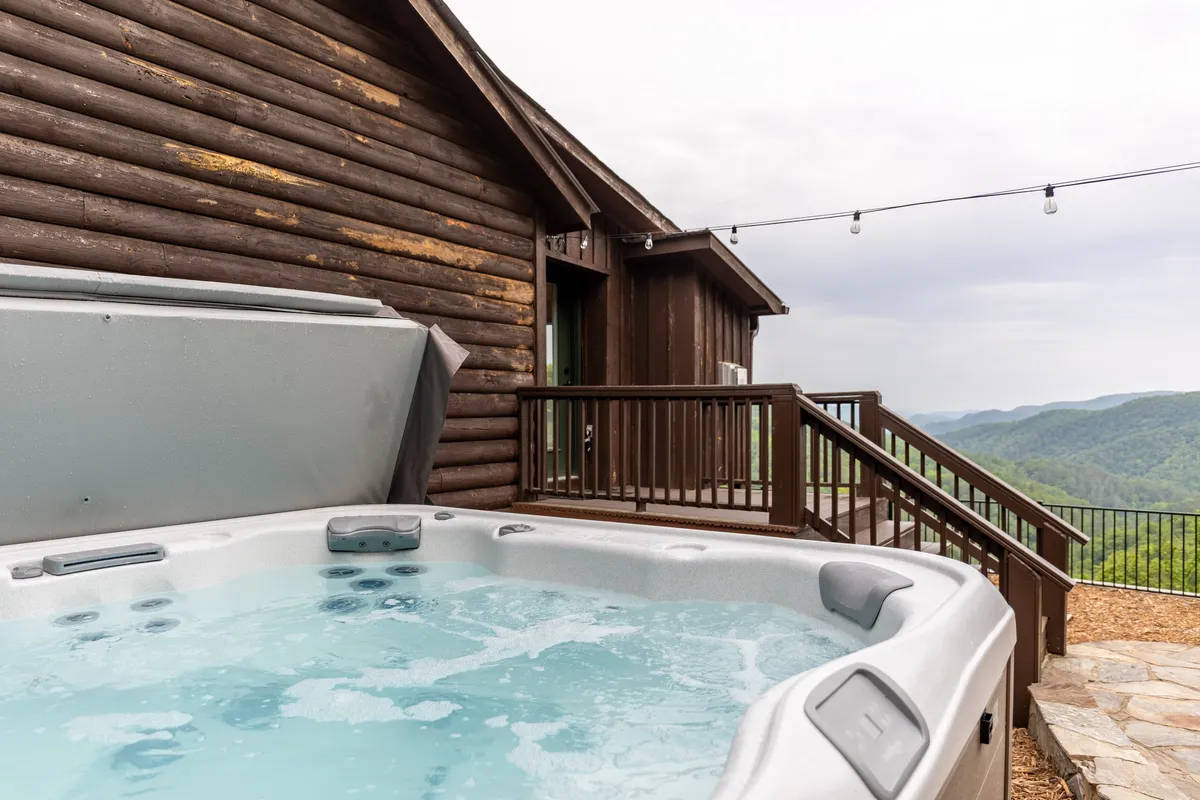 A bubbling hot tub positioned on a wooden deck, overlooking expansive mountain vistas. The scene radiates tranquility, perfect for unwinding after a day outdoors or enjoying sunset views with nature all around.