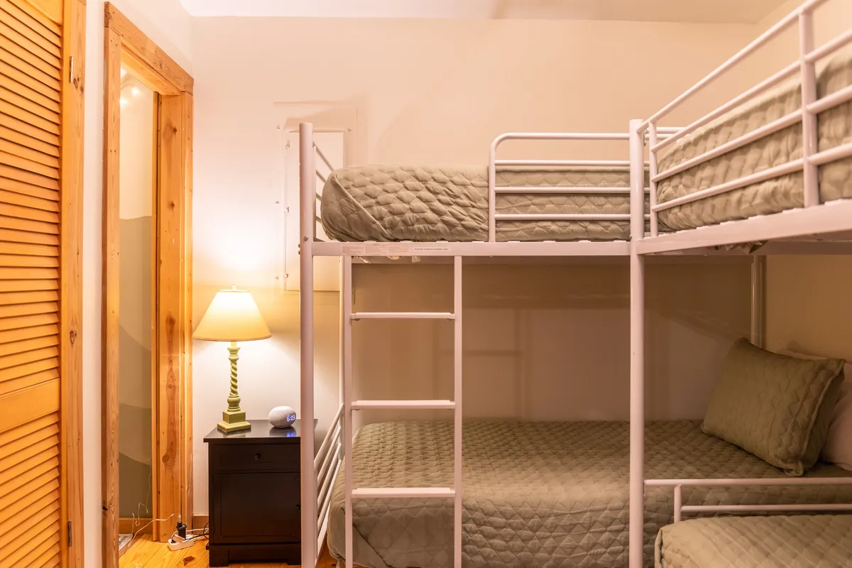 A cozy bunk room featuring stacked beds, a nightstand with a lamp, and wood accents—perfect for children to enjoy late-night chats, reading, and creating memories in their own special space.
