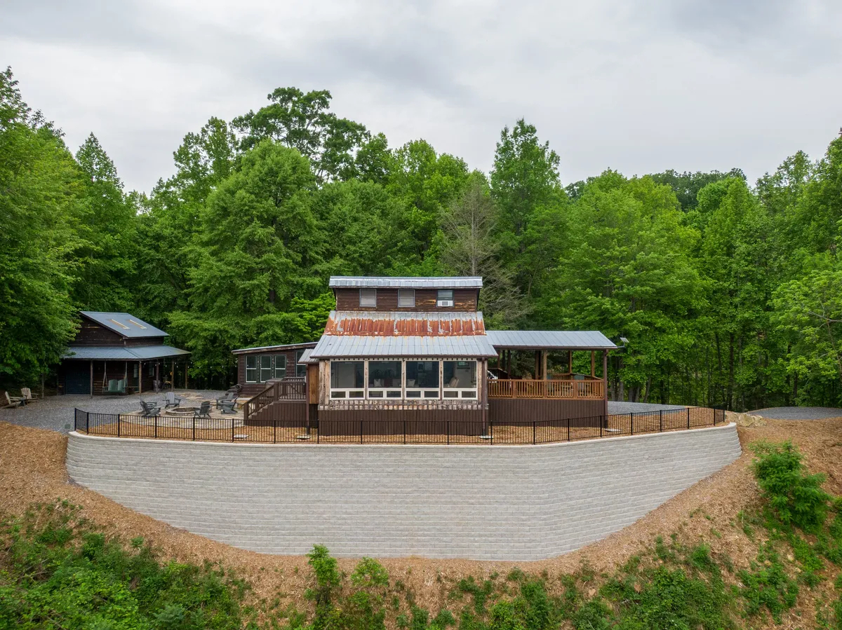 A wide exterior shot of the home, showing its rustic charm with a metal roof, a spacious deck, and lush greenery all around. The deck and surrounding outdoor spaces invite gatherings and quiet moments alike, with the mountains and trees providing a private, serene environment.