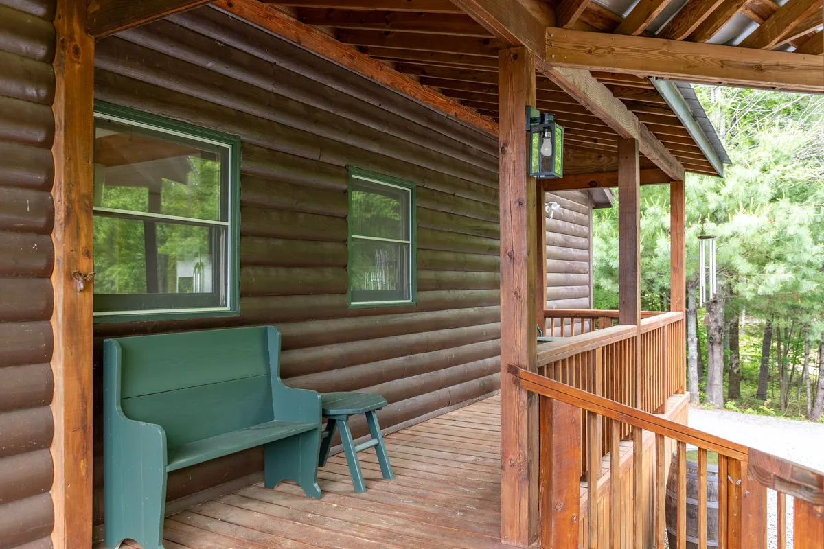 A cozy porch scene with a green bench, wooden railing, and the rustic cabin exterior visible. The setting invites relaxation, whether enjoying a sunrise coffee or gazing at the star-filled night sky from the comfort of the porch.